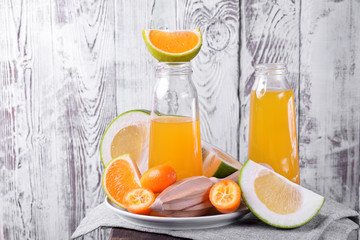 Yellow juice in glass bottles and pieces of citrus fruits against the white wooden background 