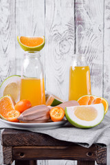 Yellow juice in glass bottles and pieces of citrus fruits against the white wooden background 
