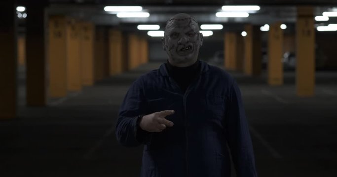 Man in jokingly dressed up in scary costume, stands in parking lot, plays paper with scissors, all Saints' holiday, Halloween night, October, scary monster, scars on his face, darkness and desolation
