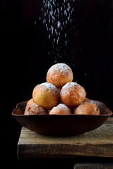 Donut balls in a clay bowl sprinkled with sugar powder on the edge of the wooden table against...