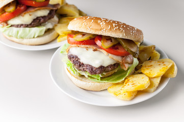 Two homemade hamburgers with a juicy meat cutlet, parmesan cheese, green salad, tomatoes and fried potatoes on a light background. Horizontal shot