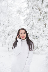 Fototapeta na wymiar Girl in a white sweater or pullover in a snowy winter park talking on the phone.