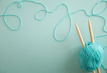 top view of colored yarn balls and knitting needles. Aquamarine background