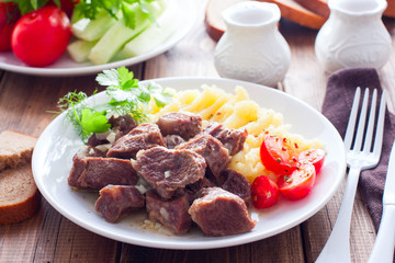 Beef stew with mashed potatoes on a white plate on a wooden table, horizontal