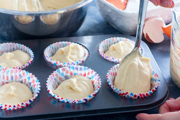 female hands spread raw cupcake dough into a metal mold, selective focus