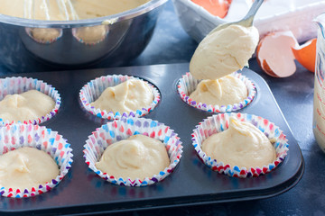 female hands spread raw cupcake dough into a metal mold, selective focus