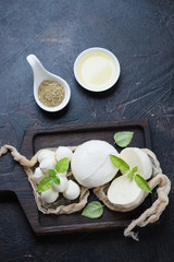 Black wooden serving tray with mozzarella cheese and green basil leaves, high angle view on a dark...