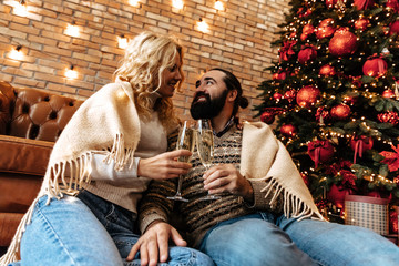 Christmas. Couple. Home. Togetherness. Man and woman are drinking champagne and smiling near the Christmas tree