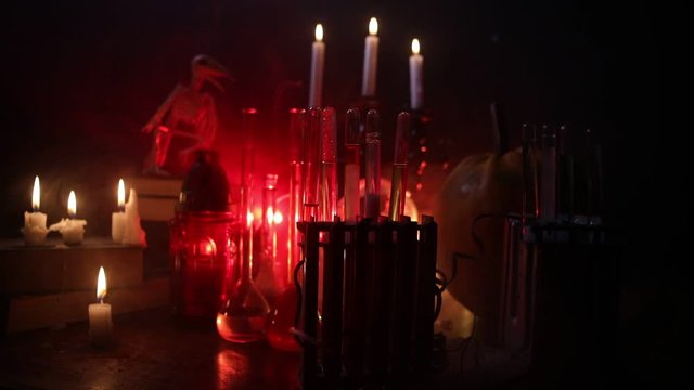 Wizard's Desk. Horror Halloween concept. Magic potions in bottles on wooden table with books and candles. Halloween still-life background with different elements on dark toned foggy background. Select