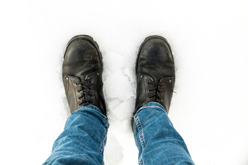 Pair of military boots and jeans still in snow covered floor during winter, taken from above