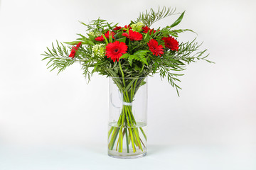 Different types of flowers arranged in a glass vase on a completely white background