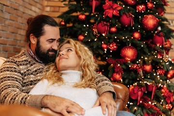 Christmas. Couple. Home. Togetherness. Man and woman are hugging and smiling near the Christmas tree