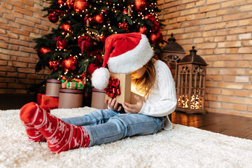 Christmas. Childhood. Presents. Home. Happy little girl is opening a gift with a light in it while sitting near the Xmas tree