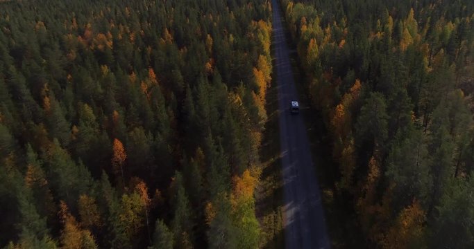 Motorhome on a forest road, Aerial, tilt down, drone shot, towards a camper van, driving on a asphalt route, in middle of fall colored trees, on a autumn day, in Pyha-Luosto national park, Finland