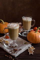 Pumpkin smoothie latte with spices in a tall glass on a wooden background in a rustic style. Autumn mood. Cookies, pumpkin, cinnamon, spices. Copy space, close-up, side view.