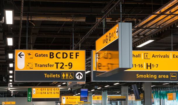 SCHIPHOL, THE NETHERLANDS – SEPTEMBER 24 2018: Various yellow illuminated direction signs at Amsterdam Airport Schiphol, the main international airport of the Netherlands.