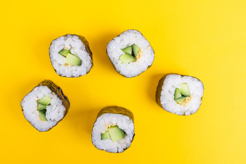 Rolls with cucumber and sesame seeds on a bright yellow background. Minimalistic concept of japanese food. Flat lay, top view. Copy space.