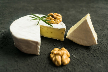Camembert cheese with herbs, decorated with a sprig of rosemary and walnut on a black background.	