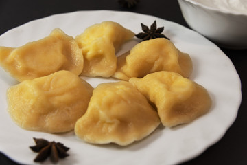 Dishes of Ukrainian national cuisine, including dumplings with fried onions and sour cream, are served in white dishes on a black background and decorated with almonds.