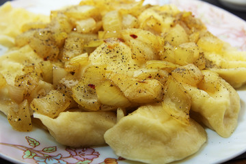 Dishes of Ukrainian national cuisine, including dumplings with fried onions and sour cream, are served in white dishes on a black background and decorated with almonds.