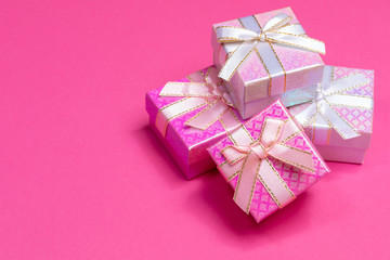 Heap of shiny gift boxes with ribbons and bows on bright pink background with copy space. 