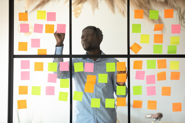 Focused african businessman checking project progress on sticky notes