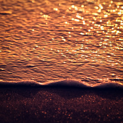 Bokeh in sand and sea waves during sunset.