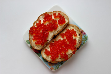Two sandwiches with red caviar on a plate with flowers. Top view