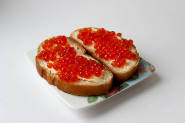 Two sandwiches with red caviar on a plate with flowers close up