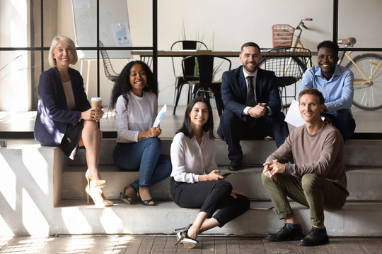 Happy diverse business team people sit on stairs in office