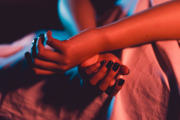 Close up on female young woman's girl's beautiful hands with black nail polish in dark room crossed...