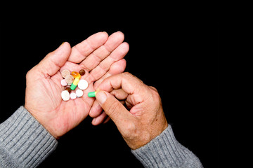 An elderly man holds many colored pills in old hands on a dark background. Painful old age. Health care for the elderly.  The View From The Top. Space for text, advertising