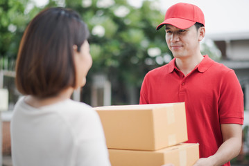 Young Asia woman receiving parcel cardboard box from post man at outdoor of home which smiling and felling happy, delivery man express shipping a goods to customer in morning.