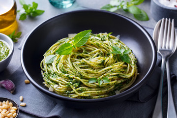 Pasta spaghetti with pesto sauce and fresh basil leaves in black bowl. Grey background. Close up. - 297116994