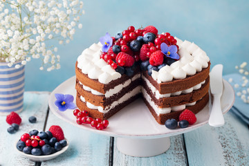 Chocolate cake with whipped cream and fresh berries. Blue wooden background. Close up.