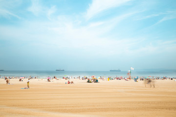 Panoramic view of sunny beach, blue cloudy sky, yellow sand and blurred people. Text space.