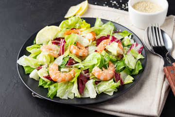 Vegetable salad with shrimp, sesame seeds, iceberg lettuce, romaine and radicchio salad on black background. Healthy food.