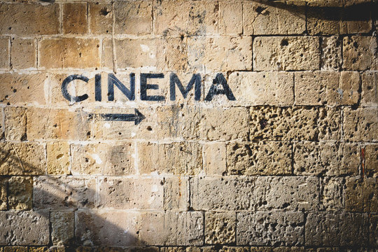 The word cinema and an arrow pointing the right side painted in black on a stone wall. Landscape format. - Powered by Adobe
