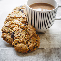 Chocolate chip cookies and a mug of tea on a white wooden table. Flat lay. Square format.