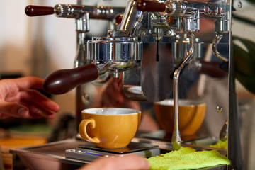 Beautiful yellow coffee cup stands on coffee machine, hands of male barista is ready to take big cup of americano, coffee house concept