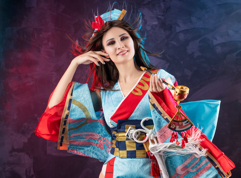 Beautiful leggy busty cosplayer girl wearing a stylized Japanese kimono costume cheerfully posing holding a fake pipe in the wind on a red and blue background.