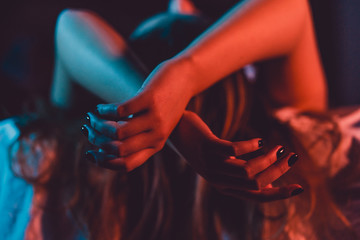 Close up on female young woman's girl's beautiful hands woman lying on the bed with black nail polish in dark room crossed fingers on sheet gentle passion love temptation emotion concept