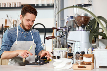 Calm serious male barista dressed in casual outfit and nice white apron, holds brush, looks down with calm face, working hard in coffee shop