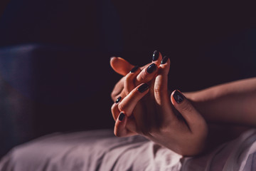 Close up on female young woman's girl's beautiful hands with black nail polish in dark room holding...