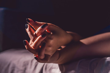 Close up on female young woman's girl's beautiful hands with black nail polish in dark room holding...