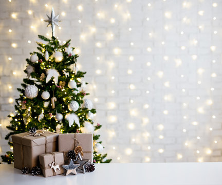 christmas and new year concept - beige gift boxes near decorated christmas tree and copy space over white brick wall