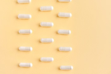 Row of medical capsules for health care with selective focus on neutral yellow background. Pharmacology supplements on yellow backdrop with empty space for text. Medicine pills. Vitamins
