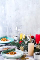 Festive Christmas and New Year table setting with dry orange and cinnamon on a gray textile. Dining place decorated with pine cones, branches and candles