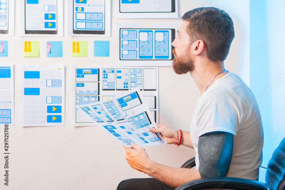 Poster a man with a beard sits in a chair and looks at the templates of program dialog boxes. the designer 
