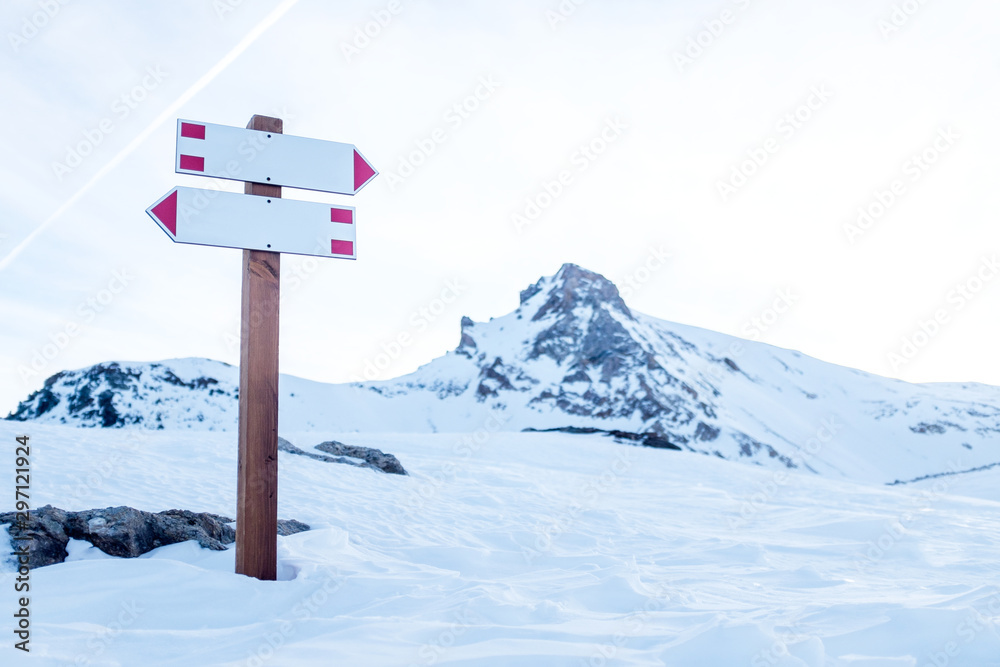 Wall mural two white signs indicating a path intersection in the mountains during winter